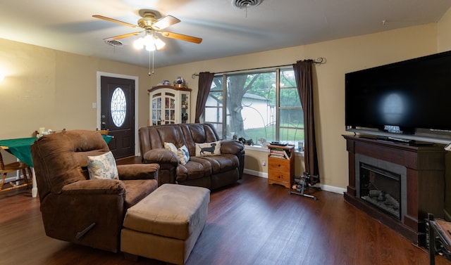 living area featuring ceiling fan, dark wood-type flooring, visible vents, baseboards, and a glass covered fireplace