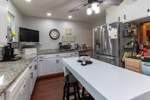 kitchen featuring ceiling fan, dark hardwood / wood-style flooring, a kitchen bar, white cabinets, and appliances with stainless steel finishes