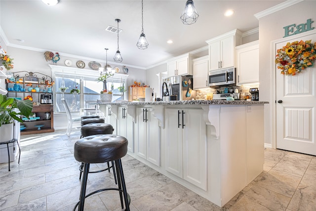 kitchen with a kitchen breakfast bar, ornamental molding, stainless steel appliances, white cabinetry, and an island with sink