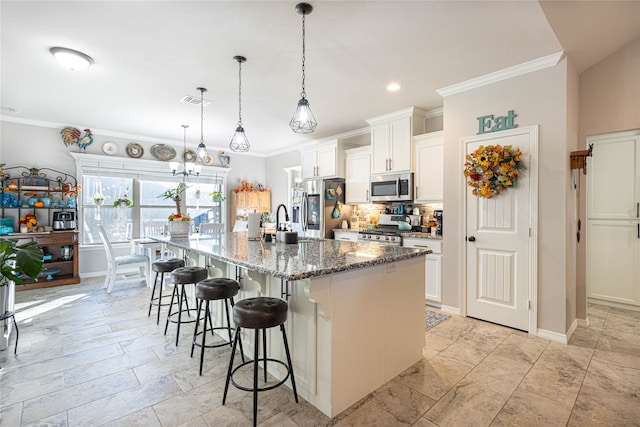 kitchen with appliances with stainless steel finishes, a kitchen breakfast bar, dark stone counters, a kitchen island with sink, and white cabinetry