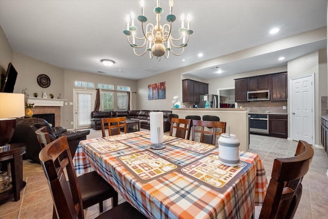 dining room featuring a tiled fireplace, light tile patterned floors, and a chandelier