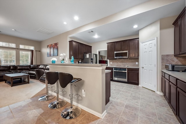 kitchen with a kitchen breakfast bar, backsplash, dark brown cabinetry, and appliances with stainless steel finishes