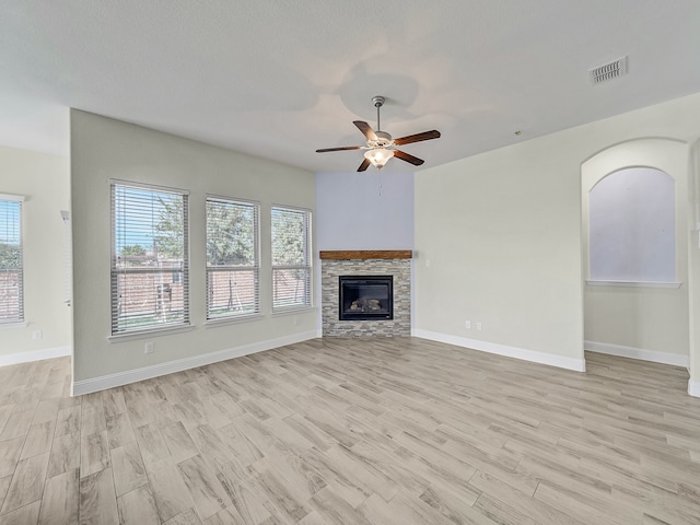 unfurnished living room with ceiling fan, a fireplace, a textured ceiling, and light wood-type flooring