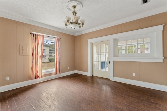 empty room with a notable chandelier, dark hardwood / wood-style flooring, ornamental molding, and a textured ceiling