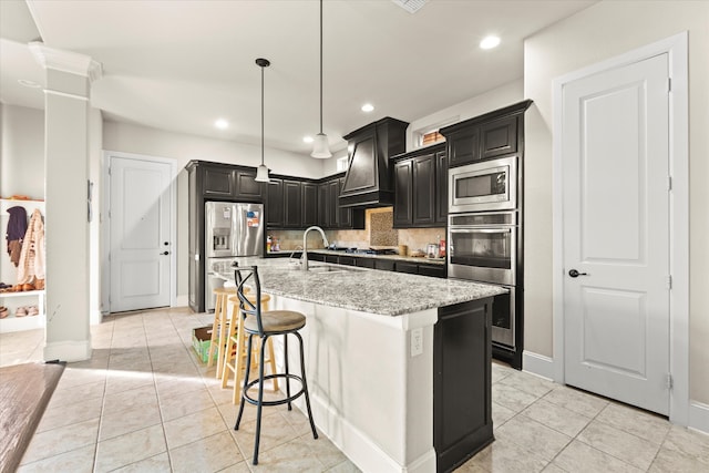 kitchen featuring a kitchen bar, custom exhaust hood, stainless steel appliances, a kitchen island with sink, and pendant lighting