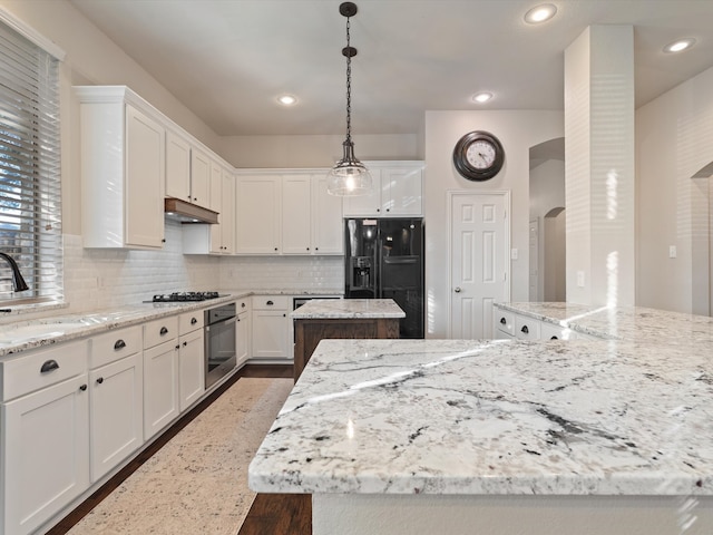 kitchen with white cabinets, light stone counters, a kitchen island, and black appliances