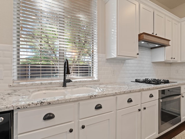 kitchen featuring premium range hood, light stone counters, sink, black appliances, and white cabinets