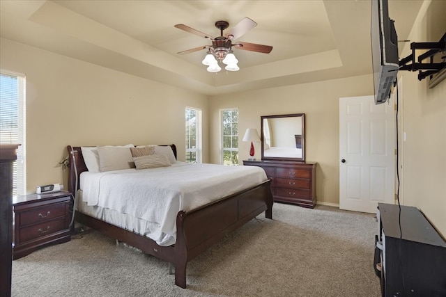 carpeted bedroom with a raised ceiling and ceiling fan