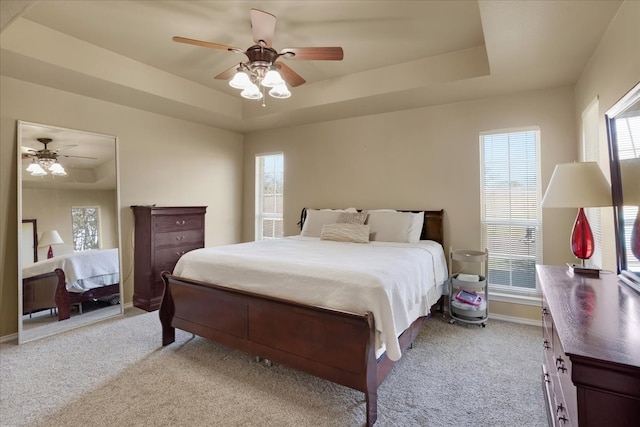 bedroom with ceiling fan, light colored carpet, and a tray ceiling