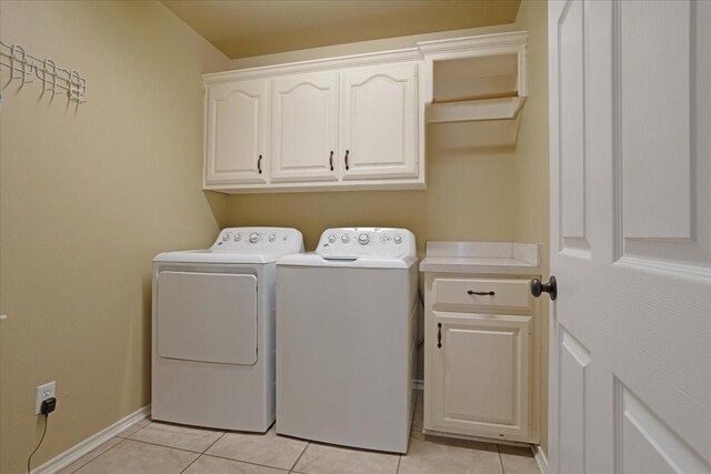 clothes washing area with washer and dryer, cabinets, and light tile patterned floors