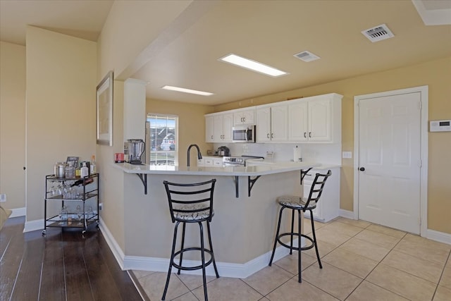 kitchen featuring stainless steel appliances, light hardwood / wood-style flooring, kitchen peninsula, a kitchen bar, and white cabinets