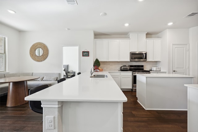 kitchen with sink, dark wood-type flooring, decorative backsplash, white cabinets, and appliances with stainless steel finishes