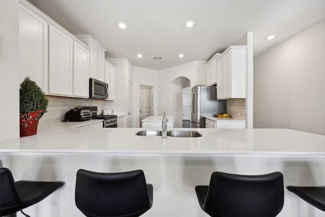 kitchen with sink, tasteful backsplash, kitchen peninsula, white cabinets, and appliances with stainless steel finishes