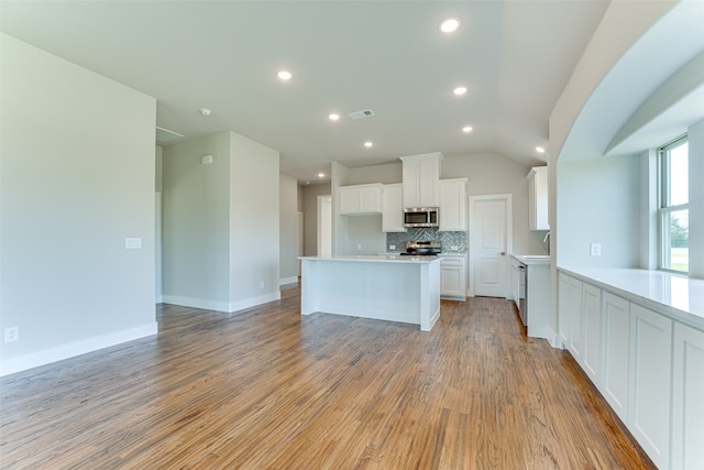 kitchen with decorative backsplash, appliances with stainless steel finishes, light wood-type flooring, vaulted ceiling, and white cabinetry