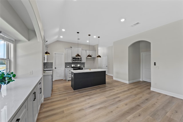 kitchen with appliances with stainless steel finishes, a kitchen island, light hardwood / wood-style flooring, white cabinetry, and hanging light fixtures