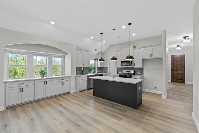 kitchen with stainless steel appliances, tasteful backsplash, pendant lighting, a kitchen island, and light wood-type flooring