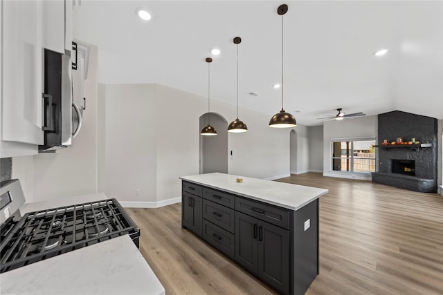 kitchen with ceiling fan, hanging light fixtures, appliances with stainless steel finishes, a kitchen island, and light wood-type flooring