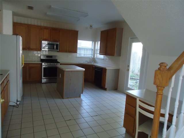 kitchen featuring sink, light tile patterned floors, appliances with stainless steel finishes, backsplash, and a center island