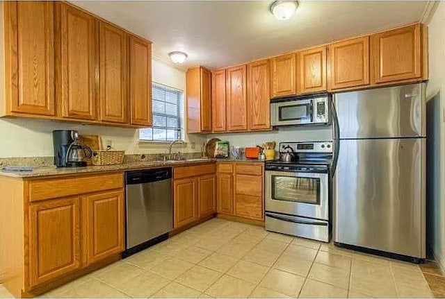 kitchen with light tile patterned flooring, appliances with stainless steel finishes, dark stone counters, and sink