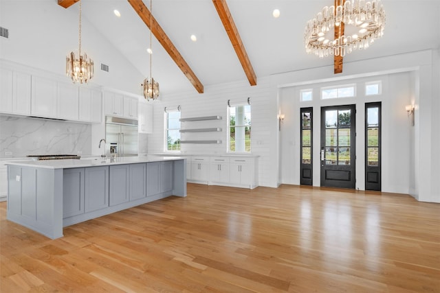 kitchen with white cabinets, high vaulted ceiling, a large island with sink, and built in refrigerator