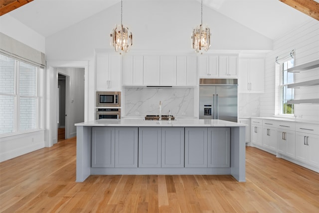 kitchen featuring beam ceiling, built in appliances, light hardwood / wood-style flooring, and an island with sink