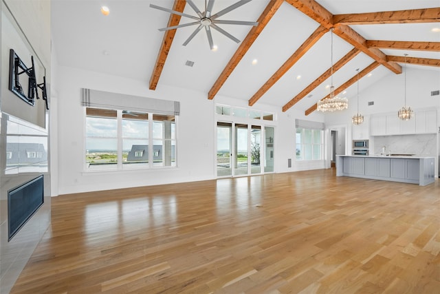 unfurnished living room with beamed ceiling, high vaulted ceiling, ceiling fan with notable chandelier, and light wood-type flooring