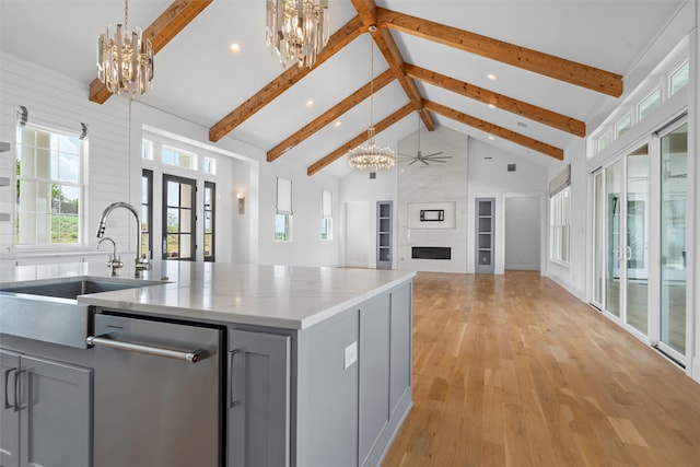 kitchen with beam ceiling, gray cabinets, a kitchen island with sink, and a large fireplace