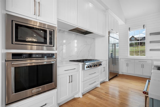 kitchen featuring tasteful backsplash, built in appliances, light hardwood / wood-style flooring, white cabinetry, and lofted ceiling