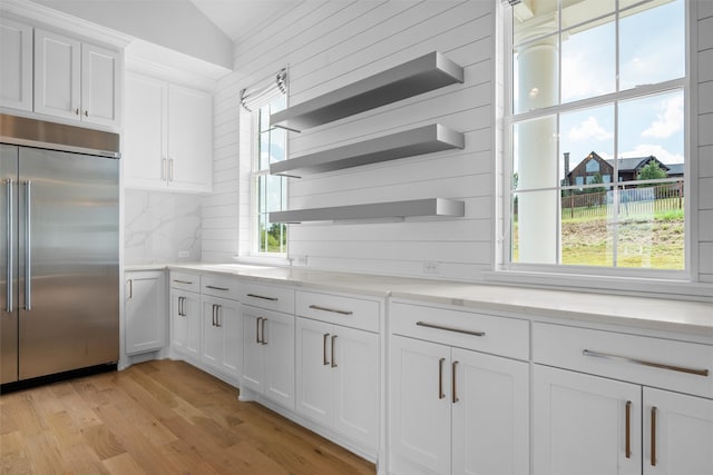 kitchen featuring decorative backsplash, stainless steel built in refrigerator, vaulted ceiling, light hardwood / wood-style floors, and white cabinetry