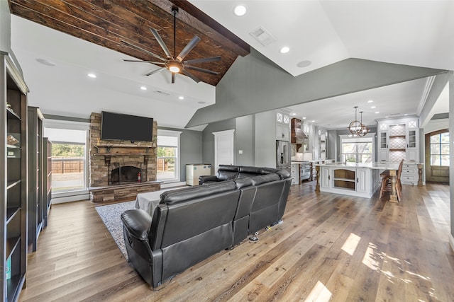 living room with ceiling fan, a stone fireplace, plenty of natural light, and light wood-type flooring