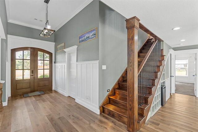 entrance foyer with ornamental molding, light hardwood / wood-style floors, and french doors