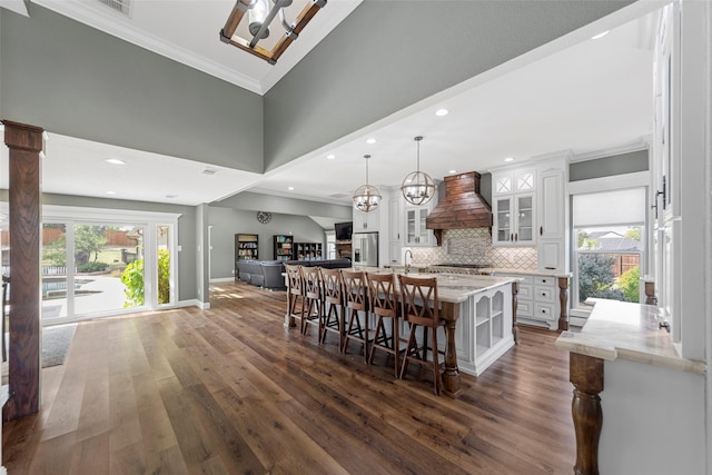 kitchen featuring premium range hood, pendant lighting, a center island with sink, and white cabinets