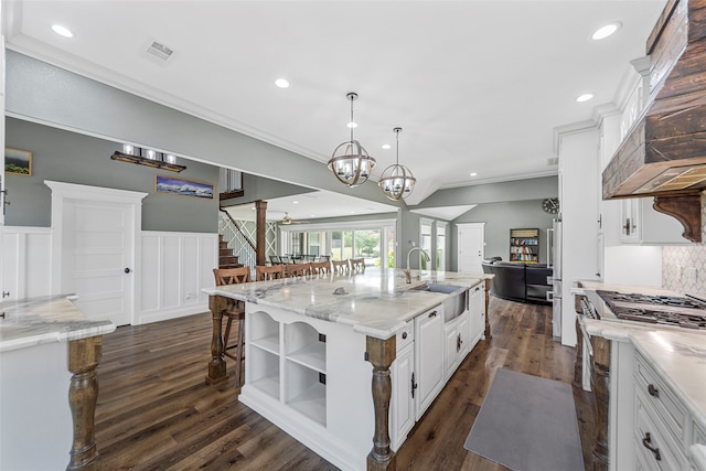 kitchen featuring sink, light stone counters, white cabinets, decorative light fixtures, and a large island with sink