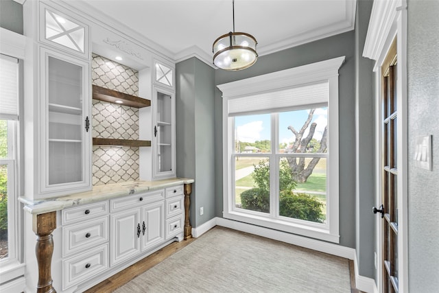 bar with white cabinetry, light stone counters, crown molding, decorative light fixtures, and light wood-type flooring