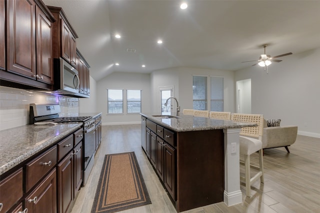 kitchen featuring sink, stainless steel appliances, light hardwood / wood-style flooring, backsplash, and a kitchen island with sink