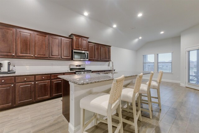 kitchen featuring light stone countertops, stainless steel appliances, light hardwood / wood-style flooring, a center island with sink, and dark brown cabinets