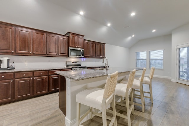 kitchen with a breakfast bar, lofted ceiling, sink, an island with sink, and appliances with stainless steel finishes