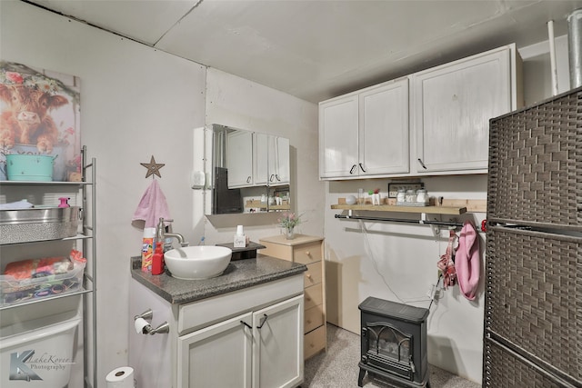 kitchen featuring a wood stove, dark stone counters, sink, light colored carpet, and white cabinetry