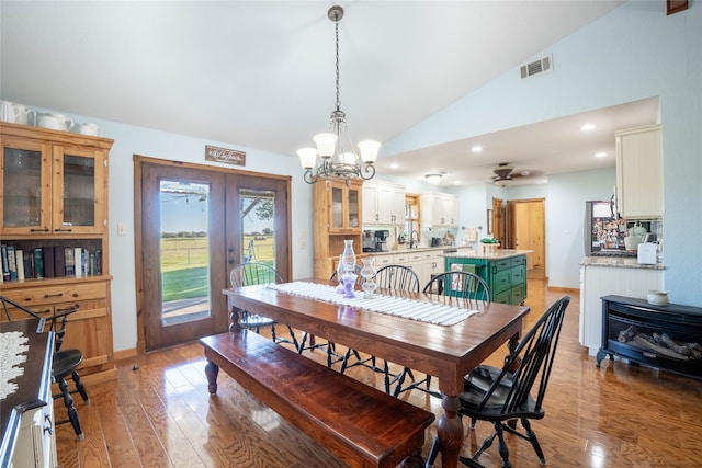 dining space featuring hardwood / wood-style floors, ceiling fan with notable chandelier, vaulted ceiling, and french doors