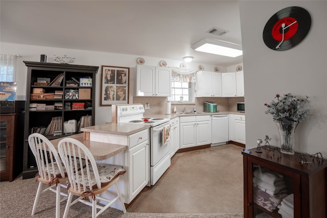 kitchen with kitchen peninsula, white appliances, tasteful backsplash, and white cabinetry