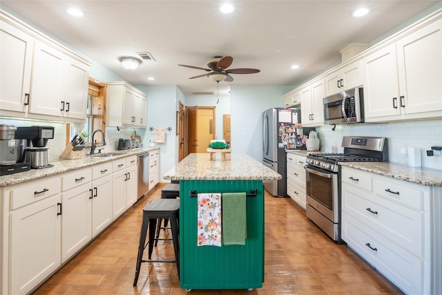 kitchen featuring a center island, white cabinets, sink, light stone countertops, and stainless steel appliances