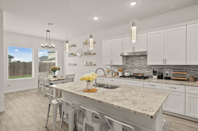 kitchen with white cabinetry, sink, hanging light fixtures, and an island with sink