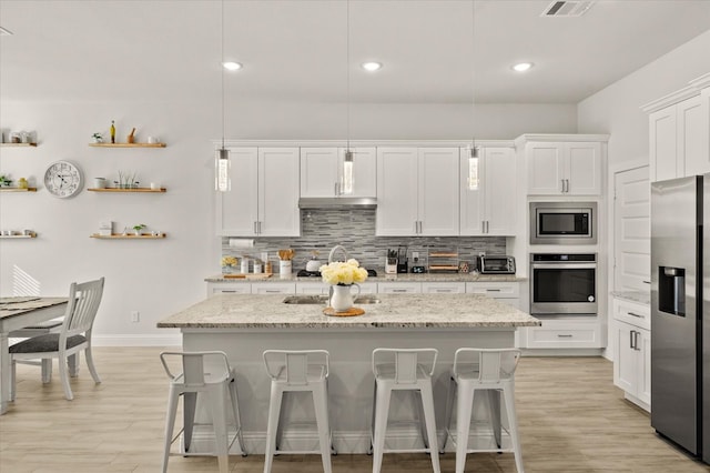 kitchen with white cabinets, pendant lighting, stainless steel appliances, and a kitchen island with sink