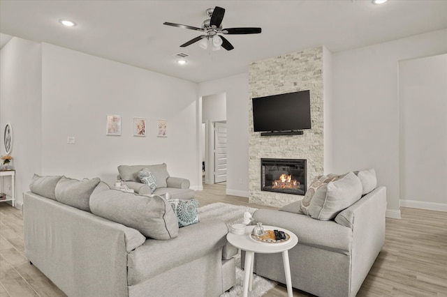 living room with a stone fireplace, ceiling fan, and light wood-type flooring