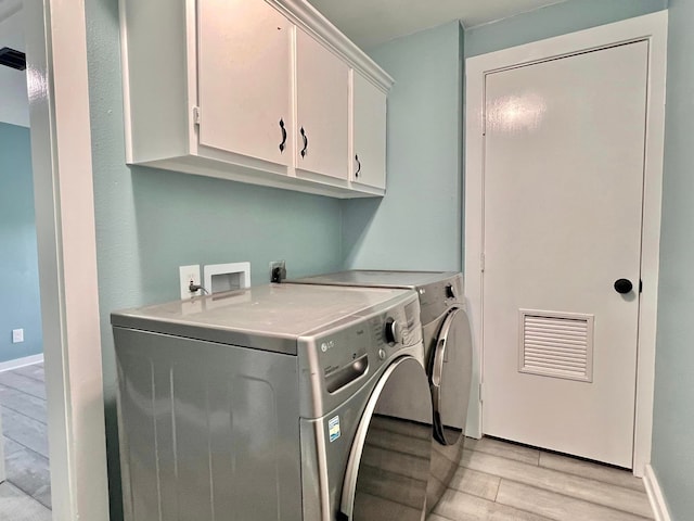 clothes washing area with washer and dryer, cabinets, and light hardwood / wood-style flooring