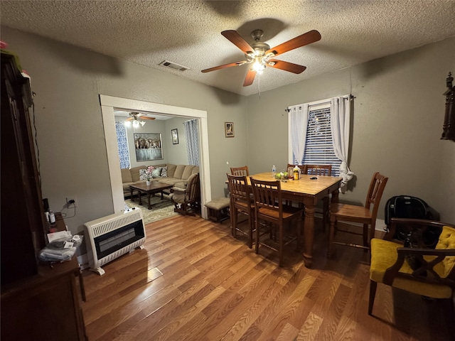 dining area featuring heating unit, ceiling fan, wood-type flooring, and a textured ceiling