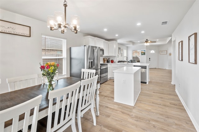 kitchen featuring kitchen peninsula, appliances with stainless steel finishes, decorative light fixtures, light hardwood / wood-style floors, and white cabinetry