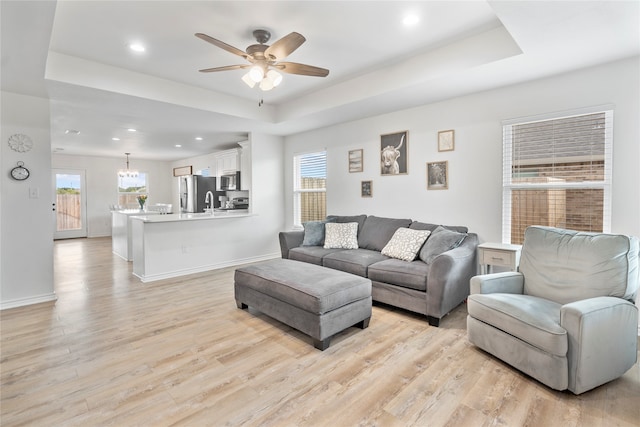 living room with plenty of natural light, a tray ceiling, and light hardwood / wood-style flooring