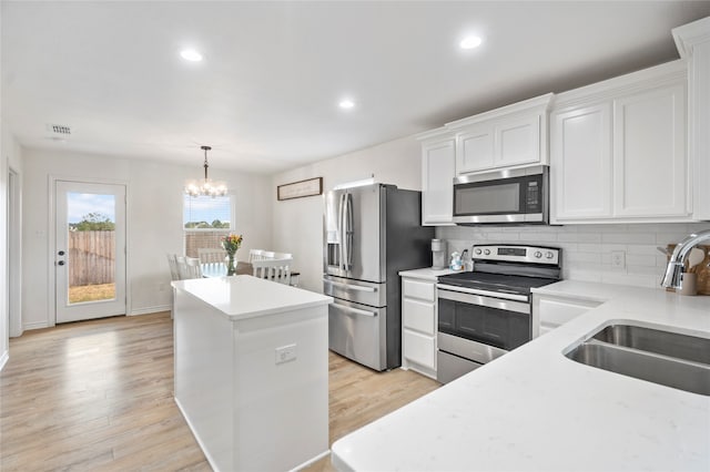 kitchen featuring appliances with stainless steel finishes, light wood-type flooring, sink, white cabinetry, and hanging light fixtures