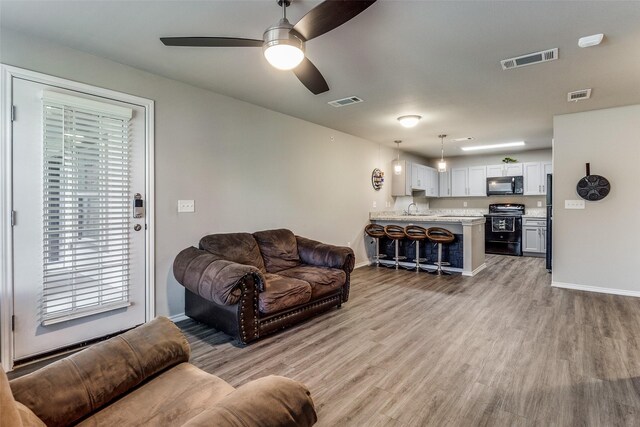 living room with ceiling fan, light wood-type flooring, and sink